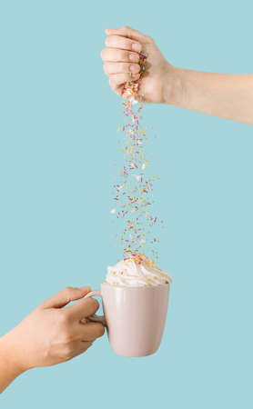 Real life composition. Two hands , one pink mug with coffee and cream. Unicorn sprinkles on colored background.の写真素材