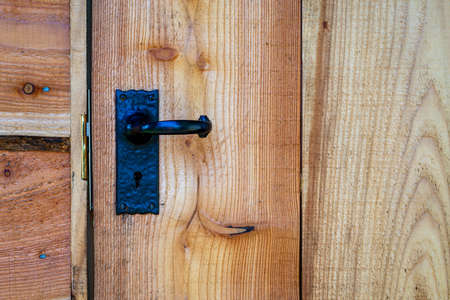 Closeup of black wrought iron door handle on waney edge wooden shed door.の写真素材