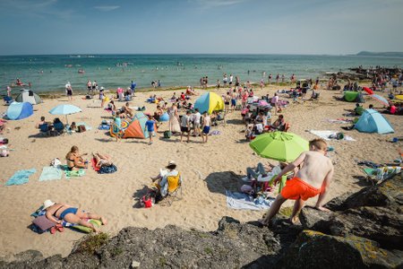 Boy climbing rocks at a busy Clonea Strand beach, County Waterford, Ireland on a hot summers day in July.のeditorial素材