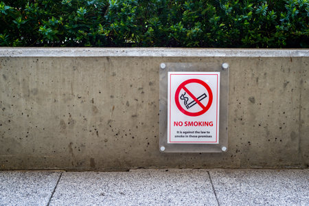 Red and white no smoking sign on wall outside near pedestrian walkway.の写真素材