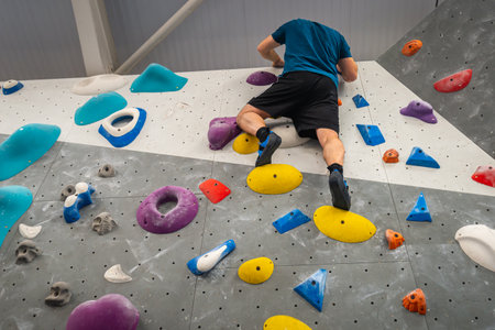 Man high up climbing indoor climbing wall using holds and grips of various shapes, sizes, colours.の写真素材