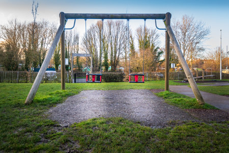 Wooden swingset in outdoor childrens playground park. Blue sky, daytime, late afternoon.