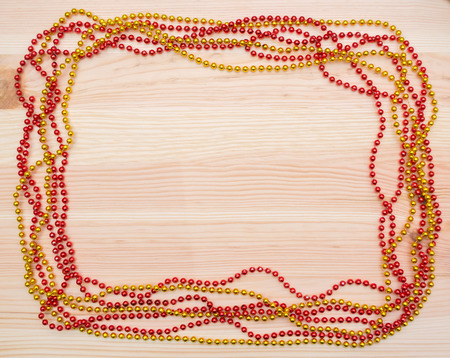 Red and gold beads on a wooden board New Year's beads. Christmas decorations. Garland. Frame of beads.の写真素材