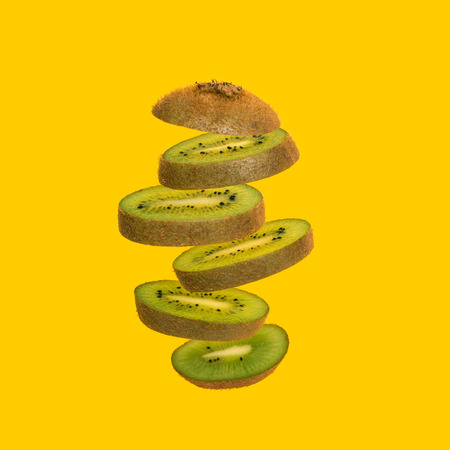 Flying kiwi. Sliced kiwi isolated on yellow background. Levity fruit floating in the air.の写真素材