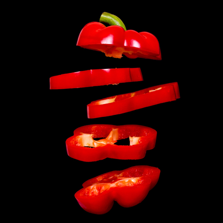Flying red paprika. Sliced floating pepper isolated. Levity capsicum vegetable isolated on black...