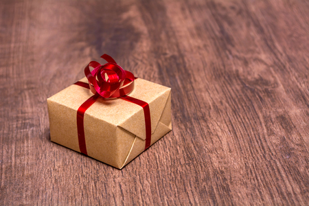 A gift, tied with a red ribbon and wrapped in kraft paper on a wooden backgroundの写真素材
