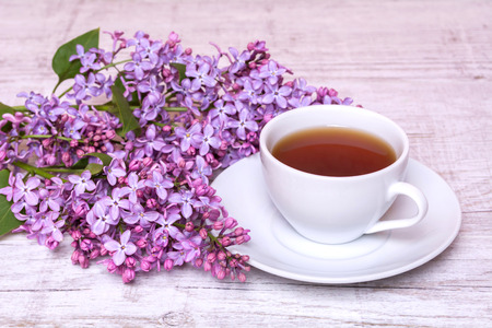 White cup with coffee or tea and a bouquet of lilacs on a wooden backgroundの写真素材