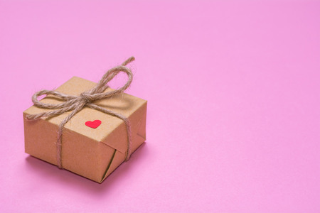 A gift wrapped in kraft paper on a pink background. Paper red heart on a gift boxの写真素材