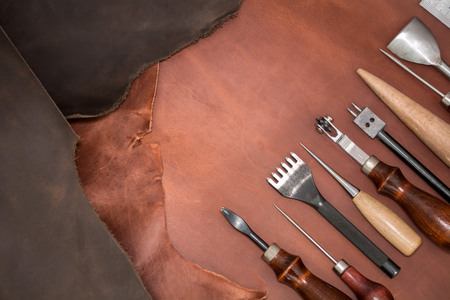 Tools for leather crafting and pieces of brown leather. Manufacture of leather goods. View from aboveの写真素材