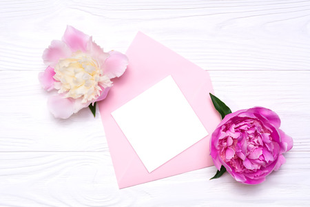 A blank note on a pink envelope. Two pink peony flowers on a white background