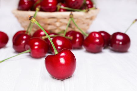 Ripe cherries in a wicker plate on a white wooden backgroundの写真素材