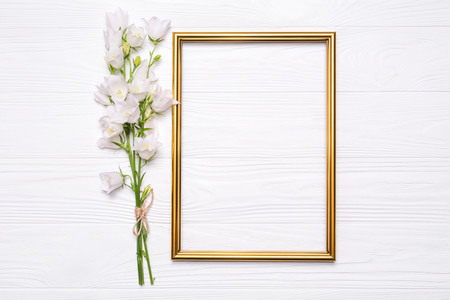 White flowers bells and a gold frame on a white wooden background. Mockup for your design