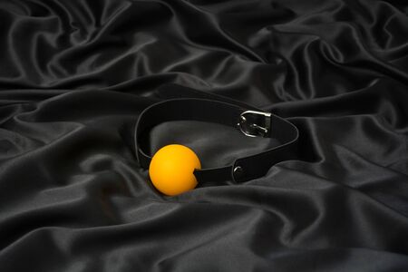 Yellow ball gag on a black silk background. Accessories for adult sexual games. Toys for BDSMの写真素材