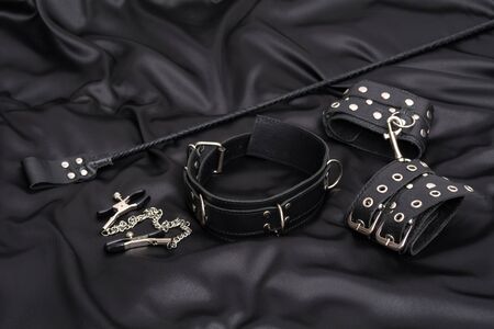Leather handcuffs, nipple clamps, chain collar and stack on black silk background. Accessories for adult sexual game. BDSM outfit.の写真素材