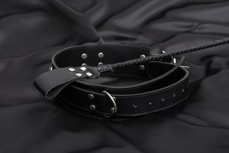 Stack for bdsm games and leather collar on black silk background. Accessories for adult sexual game. Domination conceptの写真素材