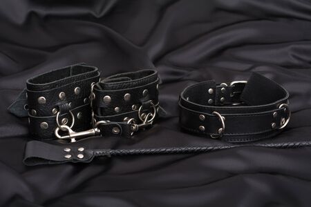 Leather handcuffs, nipple clamps, chain collar and stack on black silk background. Accessories for adult sexual game. BDSM outfit.の写真素材