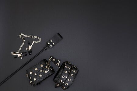 Leather handcuffs, nipple clamps and stack for BDSM games on black background. Accessories for adult sexual gameの写真素材