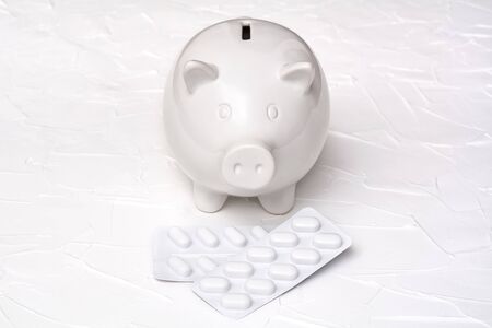 Pig piggy bank and blister of pills on a white background. Expensive healthcare costs concept