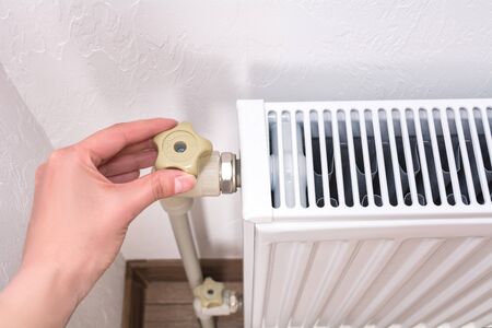 Woman hand adjusting the knob of heating radiator. Expensive heating costs conceptの写真素材