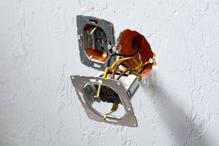 Socket plug installation. Disassembled electrical outlet in detonation wall with bare wires and...
