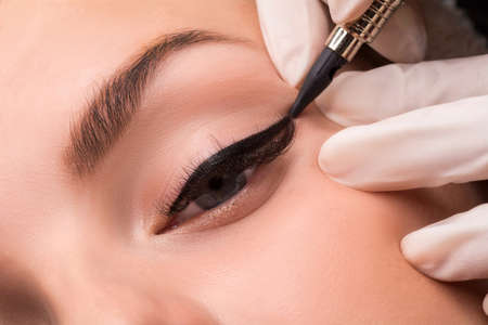 Permanent eye makeup close up shot. Cosmetologist applying tattooing of eyes. Makeup eyeliner procedure.の写真素材