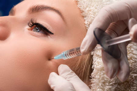 The beautician gives an injection of hyaluronic acid into the cheekbones. Injections of skin...