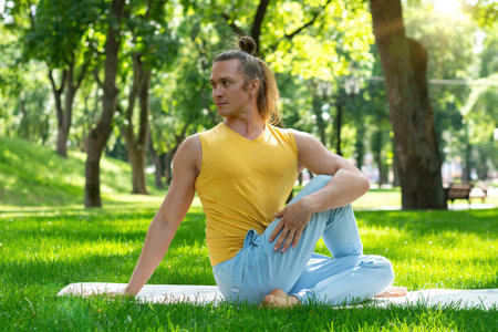 Young man practice yoga in the park. Yoga asanas in city park, sunny day. Concept of meditation,...