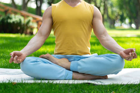 Young man practice yoga in the park. Yoga asanas in city park, sunny day. Concept of meditation, wellbeing and healthy lifestyleの写真素材