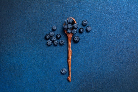 Fresh blueberries in a wooden spoon. Berries on a blue background. view from above.の写真素材