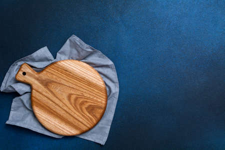 Wooden cutting board on a blue napkin on a dark blue background. Kitchenware top view. Empty space for your ready meals.の写真素材