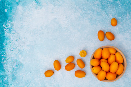 Kumquat in a wooden bowl on a blue background.