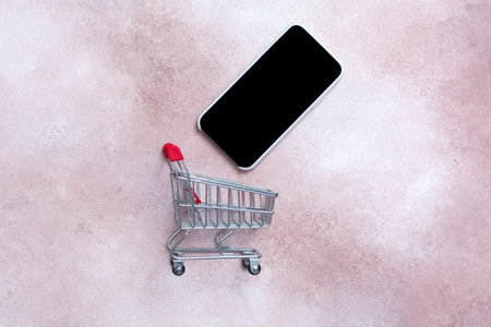 Shopping cart and smartphone on pink background, online shopping concept.の写真素材