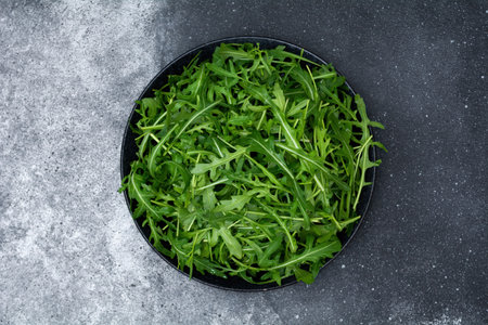 Fresh arugula leaves in bowl on stone background, top viewの写真素材