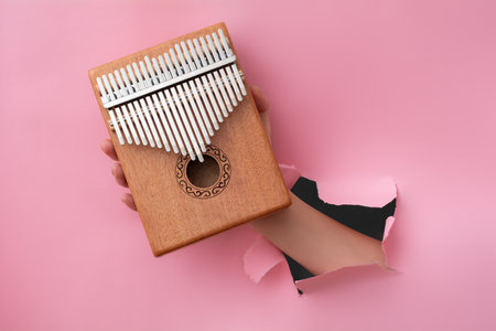 Female hand holding a kalimba through a hole in pink paperの写真素材