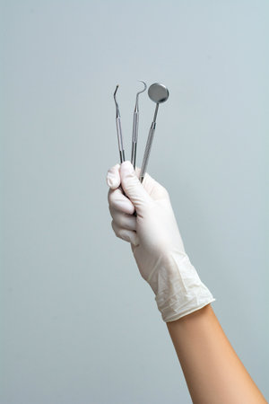 A female doctor's hand in a glove holds dental instruments on a gray background.の写真素材