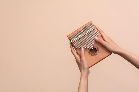 Women's hands holding a kalimba on a beige background. Wooden musical instrumentの写真素材
