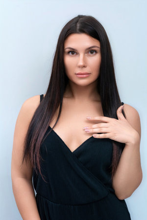 A portrait of a beautiful brunette in a black dress on a gray background. Studio photo shoot.の写真素材