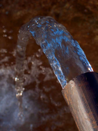 Water flowing from a flexible black plastic water pipe.の写真素材