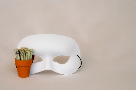 White mask next to  money in terracotta potの写真素材