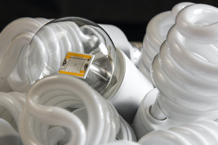 Led bulb among the many CFL lamps in front of black wallの写真素材