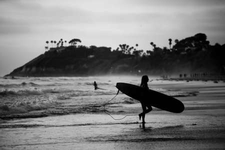 A black and white of a female surfer leaving the beach with a boardの写真素材