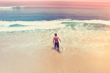Young man surfer with a surfer-board goes into the ocean, Bali, Indonesia- best place for surfing. Vintage styleの写真素材