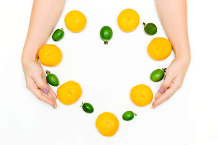 Female hands hold fresh tangerines and feijoa in shape of heart on white background. Creative love concept. Flat lay top view. Healthy organic foodの写真素材