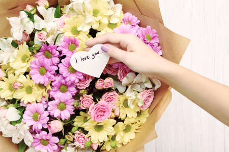 Female hand holding heart shaped greeting card with text I love you above flowers. Love and Valentine s day conceptの写真素材
