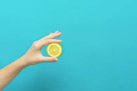 Female hand holding lemon fruit slice on blue background with copy spaceの写真素材