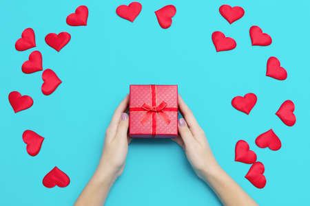 Woman hands holding red gift box on blue background with many hearts, copyspace. Valentine's Day greeting card, Happy Valentine Day background. High quality photoの写真素材