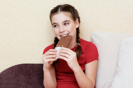 Beautiful teen girl eating chocolate bar and smilingの写真素材