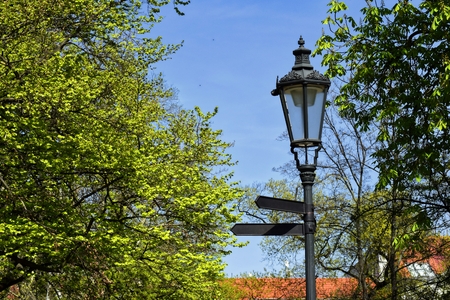 Black metal lantern with two signs in a green park. Black lantern in a green park in the background of trees and blue sky.の写真素材