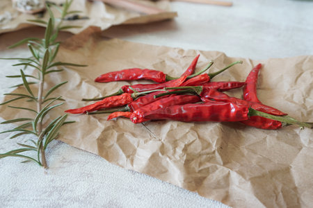 red chili peppers on a brown paper and a sprig of fresh rosemary front viewの写真素材