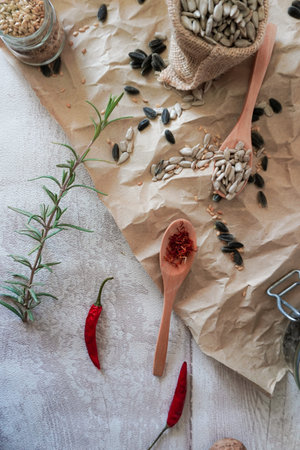 wooden spoons with sunflower seeds, saffron and flax seeds chilli peppers and rosemary on crumpled brown paperの写真素材